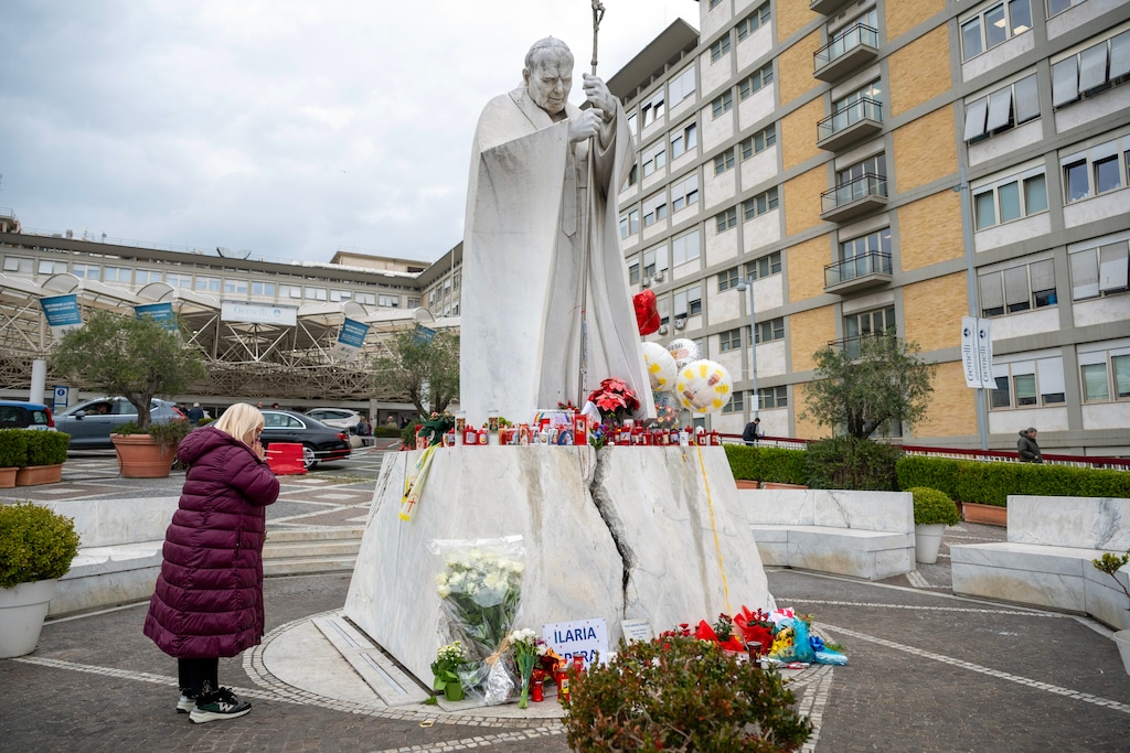 (James Hill | The New York Times) A woman prays at the statue of St. John Paul II outside Gemelli Hospital in Rome, where Pope Francis is being treated for pneumonia, a complex infection and kidney problems that have left him in critical condition, on Monday, Feb. 24, 2025. The 88-year-old pontiff was resting on Monday, the Vatican said.