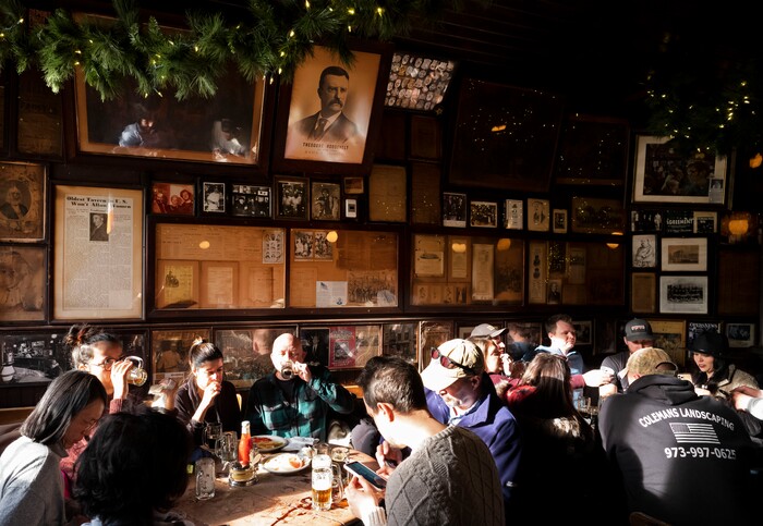 In this Dec. 27, 2019 photo, customers sit beneath vintage photos and documents, including a poster of Vice President Theodore Roosevelt, in McSorley's Old Ale House in New York. Located in Manhattan's Lower East Side, McSorley's opened in the mid-19th century and functioned as a speakeasy during Prohibition. (AP Photo/Mark Lennihan)