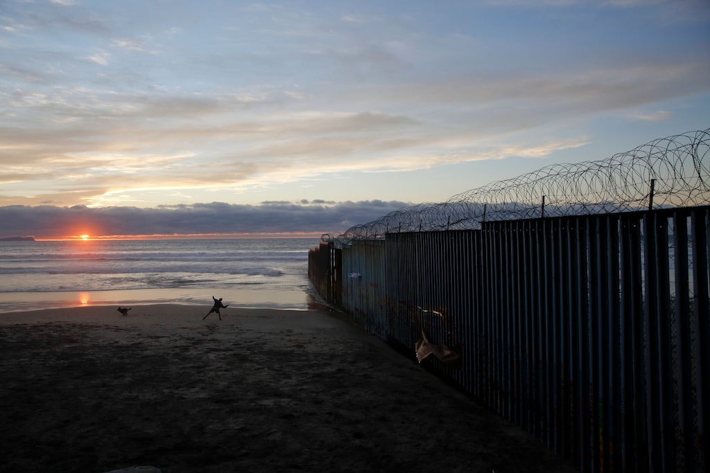 FILE - In this Jan. 9, 2019, file photo, a man throws a ball for his dog next to the border wall topped with razor wire in Tijuana, Mexico. In his demands that Congress set aside $5.7 billion for a border wall, President Donald Trump insists a physical barrier would stop heroin entering the U.S. from Mexico. But U.S. statistics, analysts and testimony at the trial of drug kingpin Joaquin "El Chapo" Guzman in New York show that most hard drugs entering the U.S. from Mexico come through land ports of entry staffed by agents, not open sections of the border. (AP Photo/Gregory Bull, File)
