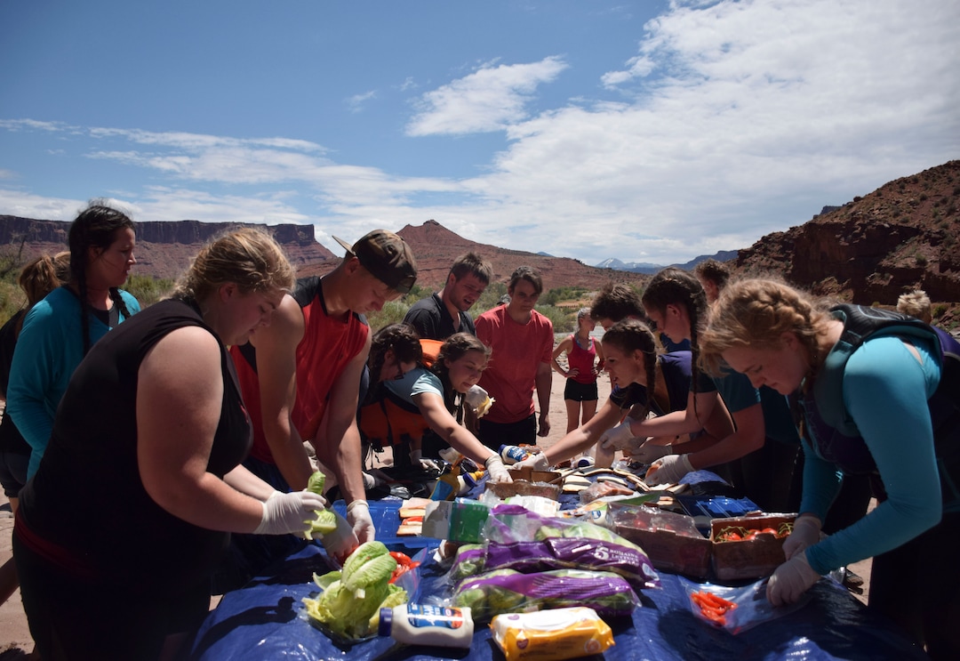 (Shannon Mullane for High Country News) Rally-goers pitch in to prepare a picnic lunch on an upside-down raft during a river trip on July 27, 2019.