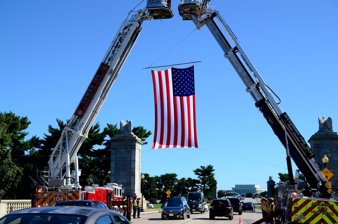 (Danny La | Special to The Tribune) The United States flag is displayed near the entrance of Arlington National Cemetery by Arlington and Alexandria fire department firefighters as they salute during the funeral procession for Staff Sgt. Taylor Hoover proceeds on Friday, Sept. 24, 2021. Hoover was killed in action due to a suicide bombing in Kabul, Afghanistan on Aug. 26.