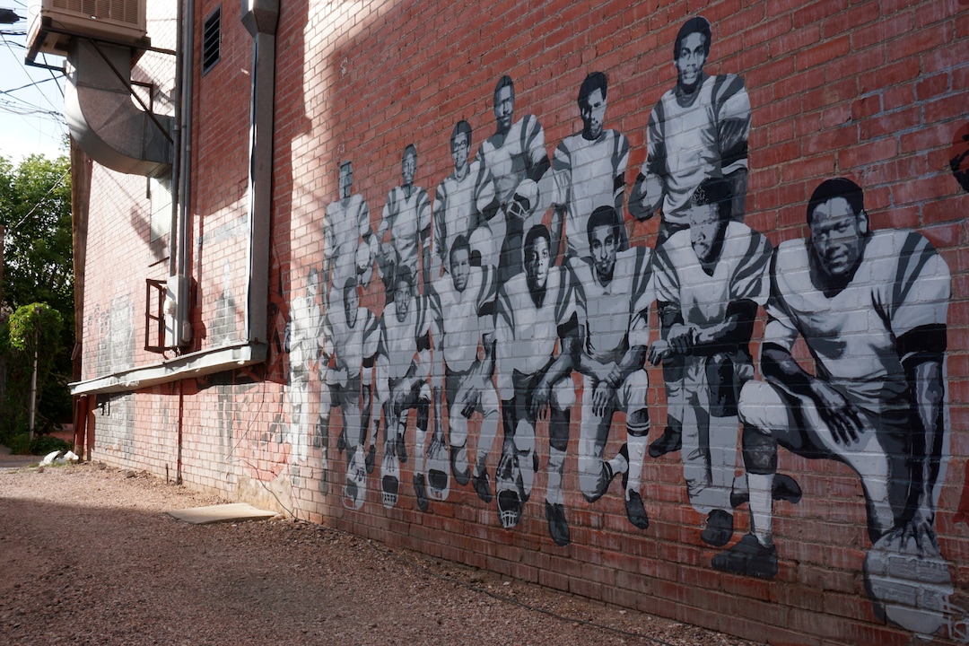 (Mead Gruver | AP Photo) In this Wednesday, Sept. 11, 2019 photo shows part of an alleyway mural in downtown Laramie, Wyo., that honors the Black 14. The Black 14 were black athletes dismissed from the University of Wyoming football team in 1969 for seeking to protest racism by wearing black armbands in a game against Brigham Young University. The university plans to dedicate a plaque honoring the group at War Memorial Stadium on Friday.