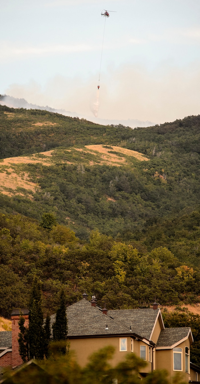 (Steve Griffin  |  The Salt Lake Tribune)  A helicopter drops a buck of water on a fire burning ridgeline  above homes in Bountiful Tuesday August 29, 2017.