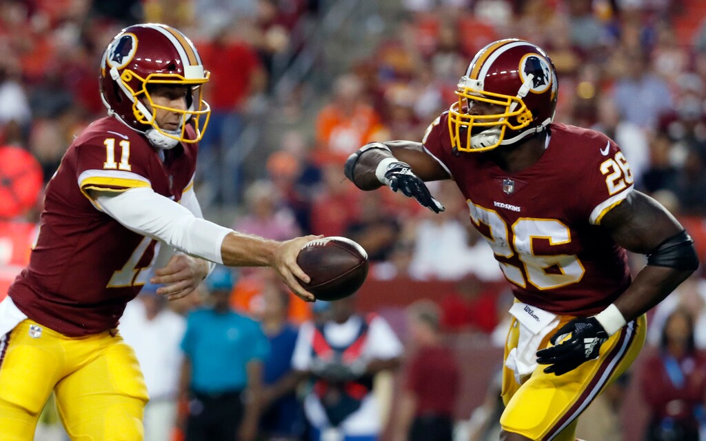 File-This Aug. 24, 2018, file photo shows Washington quarterback Alex Smith (11) handing the ball off to running back Adrian Peterson (26) during the first half of a preseason NFL football game against the Denver Broncos in Landover, Md. Smith and Peterson sat a few feet away from each other as fresh-faced college players at the Heisman Trophy ceremony in New York in late 2005 and never imaged this would happen. Twelve NFL seasons later for Smith and 11 for Peterson and they’re now in the same backfield together with Washington.  (AP Photo/Alex Brandon, File)