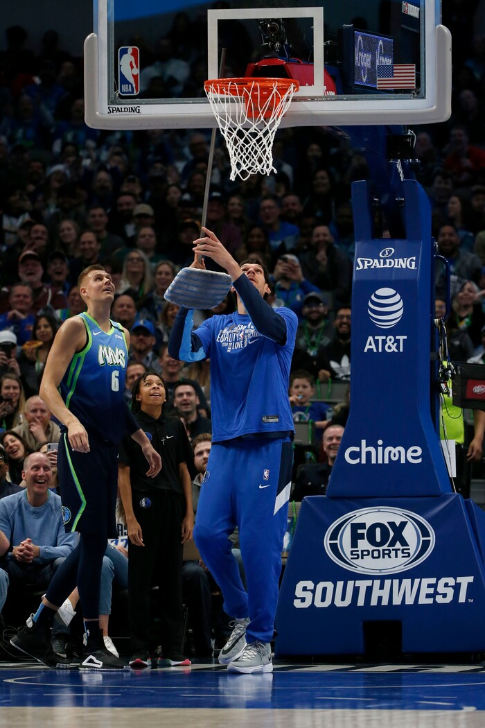 Dallas Mavericks forward Kristaps Porzingis (6) watches as center Boban Marjanovic uses a broom to poke the ball from the backboard as they played the Utah Jazz during the first half an NBA basketball game in Dallas, Monday, Feb. 10, 2020. (AP Photo/Michael Ainsworth)