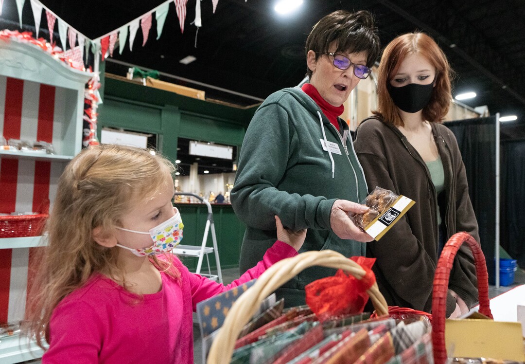 (Francisco Kjolseth | The Salt Lake Tribune) Patti Peterson of Las Vegas is joined by her grandchildren Dot, 5, and Liz Peterson, 15, within the wall of the Elf Emporium store front that was built by her family in her honor for the 51st Festival of Trees at the Mountain America Expo Center in Sandy on Tuesday, Nov. 30, 2021. Patti who has terminal cancer and developed a community of friends through her treatments and service to others says, “My cancer journey has been joyful because I wasn’t always thinking about myself.”