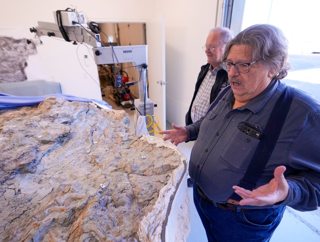 (Bethany Baker | The Salt Lake Tribune) James Kirkland, right, the Utah state paleontologist, and Bill Keach, the state geologist, explain the significance of the Utahraptor megablock at the core center for the Utah Department of Natural Resources in Salt Lake City on Monday, Jan. 29, 2024. The 9-ton piece of rock contains more than a dozen raptor skeletons that date back 135 million years, but state resource managers are having trouble securing funding to excavate the fossils.