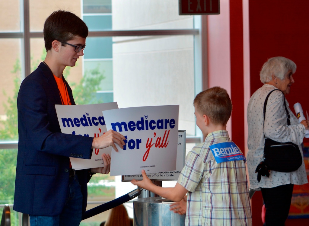 A volunteer hands out a poster as Vermont independent Sen. Bernie Sanders was set to address a “Medicare for All” rally in downtown Columbia, S.C. on Saturday, Oct. 20, 2018.  Sanders hasn’t announced intentions for another bid in 2020. But in the run-up to the Nov. 6 election, he’s visiting more than half a dozen states to stump with congressional candidates. (AP Photo/Meg Kinnard).