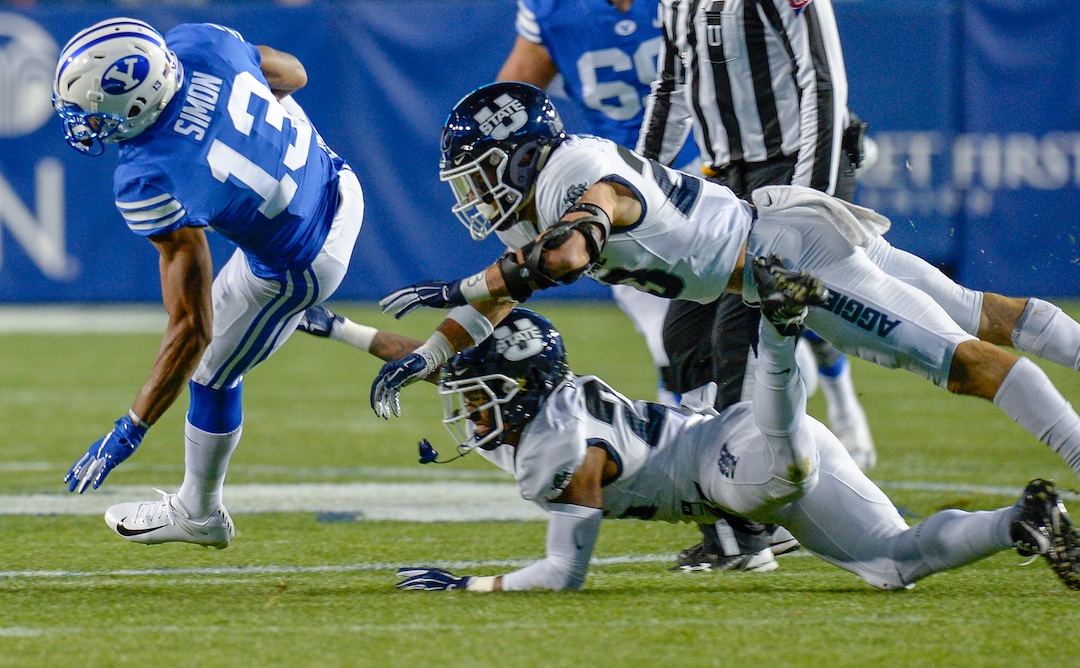 Leah Hogsten  |  The Salt Lake Tribune  Brigham Young Cougars wide receiver Micah Simon (13) is brought down by Utah State Aggies safety Gaje Ferguson (23) and Utah State Aggies defensive end Dalton Baker (24) as BYU hosts Utah State University at Lavell Edwards Stadium in Provo, Friday, Oct. 5, 2018.