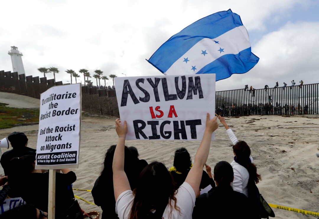 (Chris Carlson | The Associated Press)  Central American migrants sit on top of the border wall on the beach in San Diego during a gathering of migrants living on both sides of the border, Sunday, April 29, 2018.
