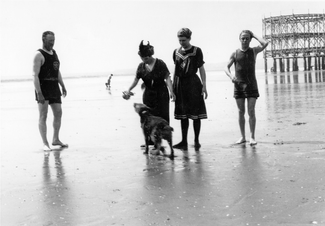 (Utah State Historical Society) A family pauses for a photograph while playing with their dog on the beach of the Great Salt Lake near the original Saltair. The figure 8 roller coaster, at right, premiered at the resort in 1914.