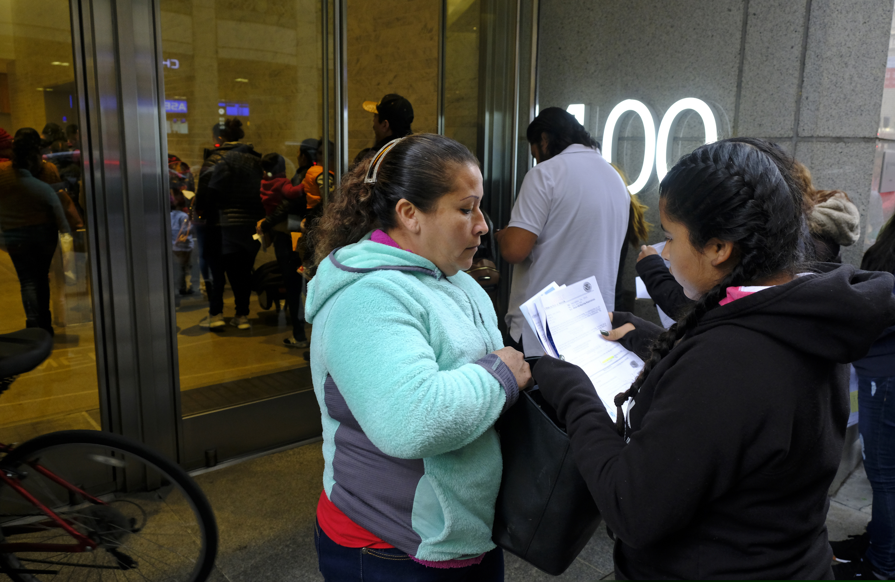 (AP Photo/Eric Risberg) Two women look over their documents by a line snaking around the block outside a U.S. immigration office with numerous courtrooms Thursday, Jan. 31, 2019, in San Francisco. The crowd was mixed with people who had court appointments for Thursday, people whose appointments were swallowed up by shutdown and others who had 'Notices to Appear' but assumed that meant they had court dates.