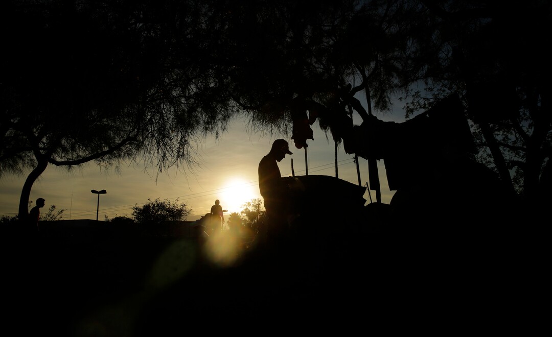 In this Tuesday, Nov. 5, 2019, photo, immigrants waiting for their U.S. court dates live in a refugee camp in Matamoros, Mexico, cooks dinner as the sun sets. The camp is an outgrowth of the Trump administration’s “Remain in Mexico” program, in which more than 55,000 migrants seeking entry into the U.S. have been ordered to pursue their cases outside its borders. (AP Photo/Eric Gay)