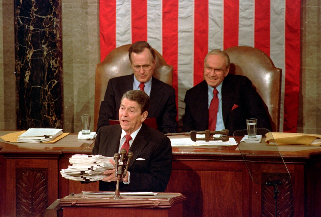 (Bob Daugherty | AP file photo) Then-President Ronald Reagan holds up 14-pound continuing resolution for the budget, part of a total package weighing 43-pounds, which the president said was two months late from Congress, during his State of the Union address on Capitol Hill in Washington on Jan. 25, 1988. Then-Vice President George H.W. Bush, left, and then-House Speaker James Wright of Texas listen behind him.