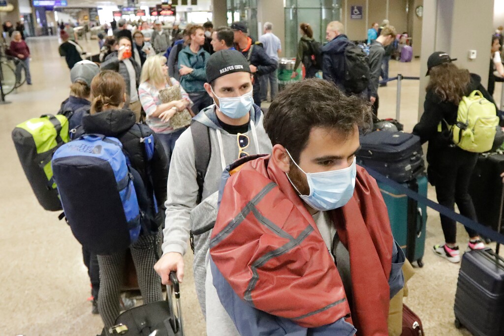 (Rick Bowmer | AP photo)
Masked travelers stand in line with luggage before getting to the ticket counter at the Salt Lake City International Airport Sunday, March 15, 2020, in Salt Lake City. For most people, the new coronavirus causes only mild or moderate symptoms, such as fever and cough. For some, especially older adults and people with existing health problems, it can cause more severe illness, including pneumonia.