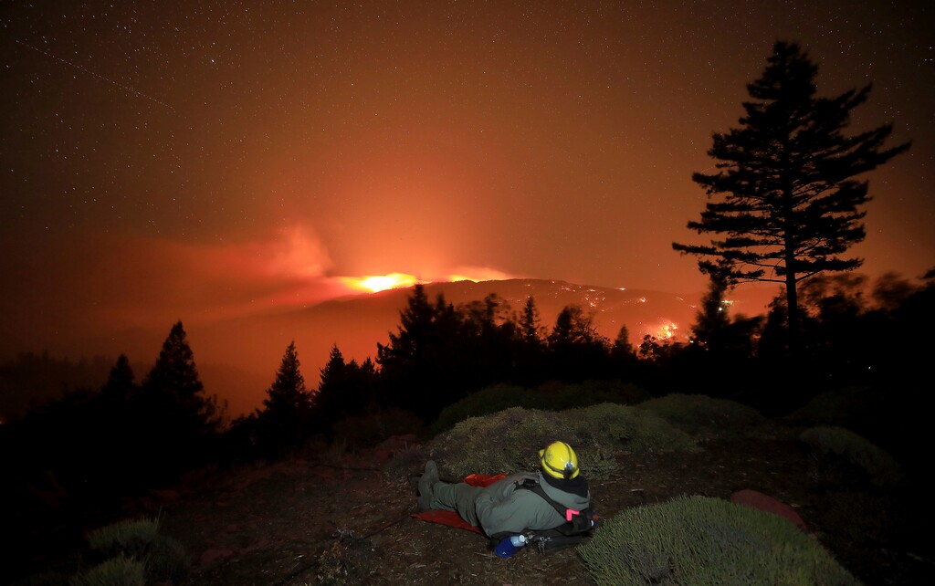 Firefighter Alex DeLeon, of South Lake Tahoe, Calif., bundles up against the cold wind on a ridge between Sonoma and Lake County as the Kincade fire burns, Tuesday, Oct. 29, 2019, in northern California. The flames prompted a flurry of false fire reports on the Santa Rosa plain. (Kent Porter/The Press Democrat via AP)