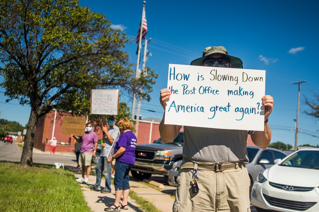 (Katy Kildee | Midland Daily News via AP file photo)  Eric Severson holds a sign as a few dozen people gather in front of the United States Post Office on Rodd St. to protest recent changes to the U.S. Postal Service under new Postmaster General Louis DeJoy Tuesday, Aug. 11, 2020 in Midland, Mich.