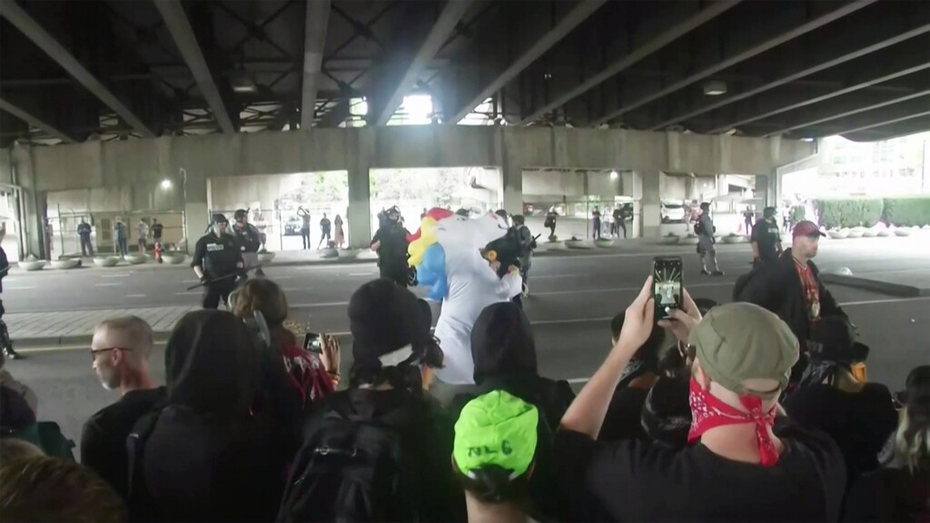 (APTN | AP Photo) Portland police riot gear watch counterprotesters gathered in downtown Portland, Ore., on Saturday, Aug. 17, 2019. Police seized weapons such as bear spray and shields as right-wing groups and counterprotesters gathered on Saturday. Authorities also set up concrete barriers and closed streets in an effort to contain the groups.