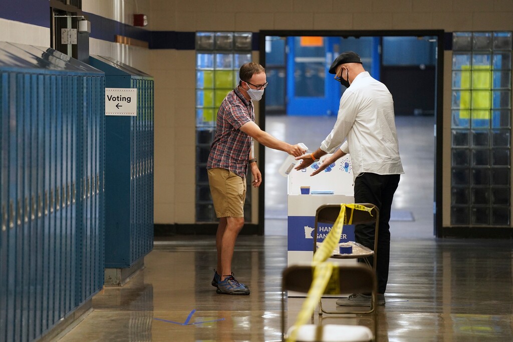 (Anthony Souffle | Star Tribune via AP file photo) Election judge Tyler Sahnow, left, sprays hand sanitizer to John Enloe as he arrives to vote at Northeast Middle School in Minneapolis, Minnesota, during the first election in Minnesota since the full outbreak of the COVID-19 pandemic, Tuesday, Aug. 11, 2020.