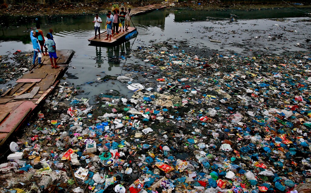 (Rafiq Maqbool | AP file photo) A man guides a raft through a polluted canal littered with plastic bags and other garbage in Mumbai, India, in October 2016. United Nations officials say nearly all of the world's countries have agreed on a deal to better manage plastic waste, with the United States a notable exception.