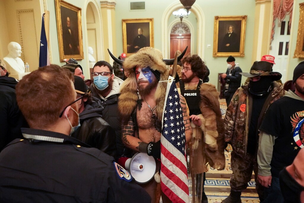 (Erin Schaff | The New York Times)
Jacob Anthony Chansley, center, a QAnon adherent known as the Q Shaman, with other supporters of President Donald Trump who swarmed the U.S. Capitol, confronting Capitol Police officers in the building, in Washington, Jan. 6, 2021. They came from around the country, with different affiliations — QAnon, Proud Boys, a few elected officials, many everyday Americans. One allegiance united them.