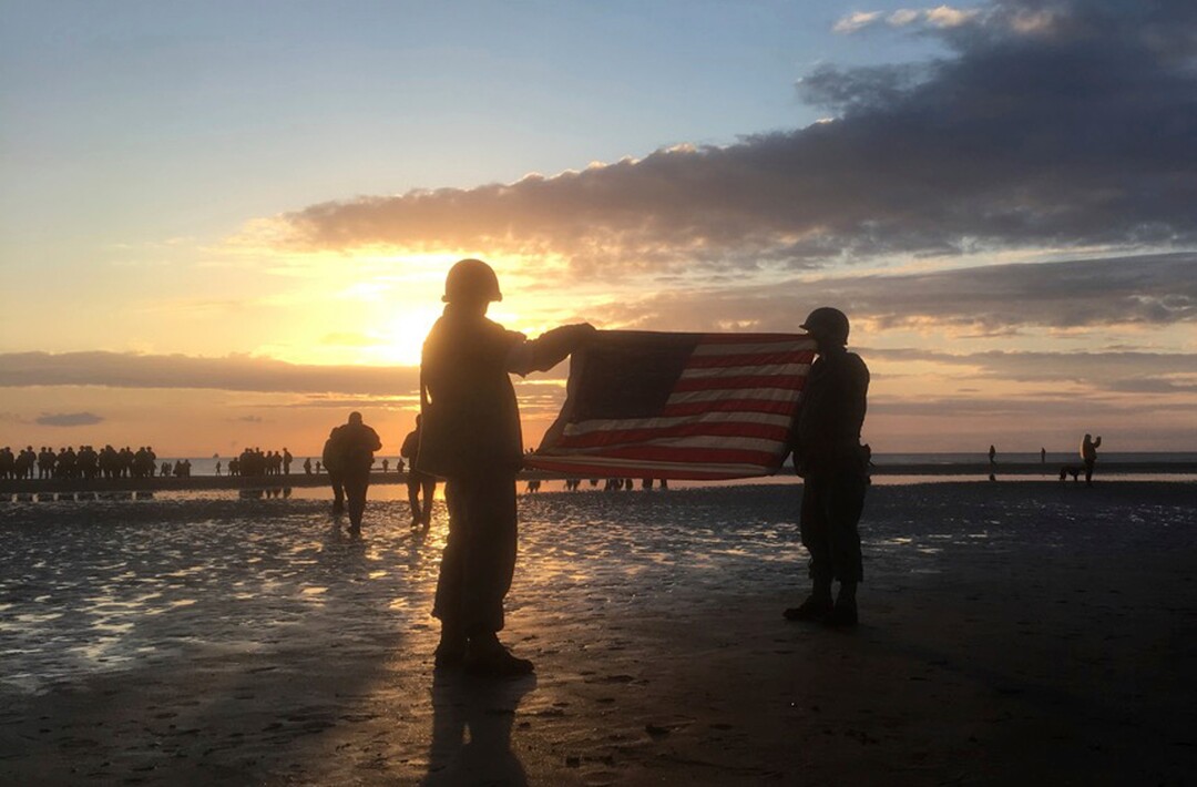 (Maxence Piel via AP) Re-enactors hold an American flag at sunrise as part of events to mark the 75th anniversary of D-Day on Omaha Beach in Vierville-sur-Mer, Normandy, France, Thursday, June 6, 2019. World leaders are gathered Thursday in France to mark the 75th anniversary of the D-Day landings.