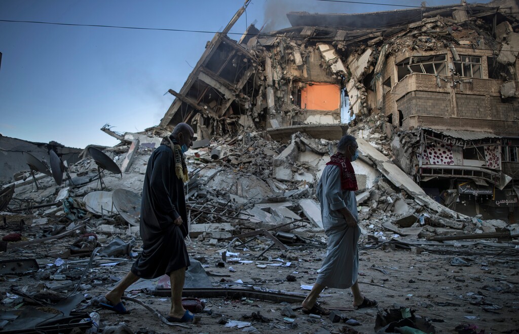 (AP Photo/Khalil Hamra) Palestinians walk next to the remains of a destroyed 15 story building after being hit by Israeli airstrikes on Gaza City, Thursday, May 13, 2021.
