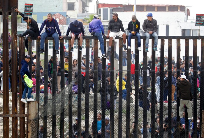 (Chris Carlson | The Associated Press)  Central American migrants sit on top of the border wall on the beach during a gathering of migrants living on both sides of the border, Sunday, April 29, 2018, in San Diego.