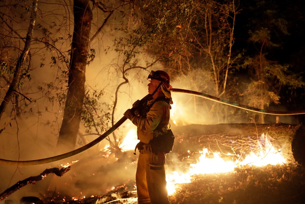 (AP Photo/Marcio Jose Sanchez, File) In this Oct. 14, 2017 file photo, a firefighter holds a water hose while fighting a wildfire in Santa Rosa, Calif. Investigators say the deadly 2017 wildfire that killed 22 people in California's wine country was caused by a private electrical system, not embattled Pacific Gas & Electric Co. The state's firefighting agency said Thursday, Jan. 24, 2019, that the Tubbs Fire started next to a residence. They did not find any violations of state law.