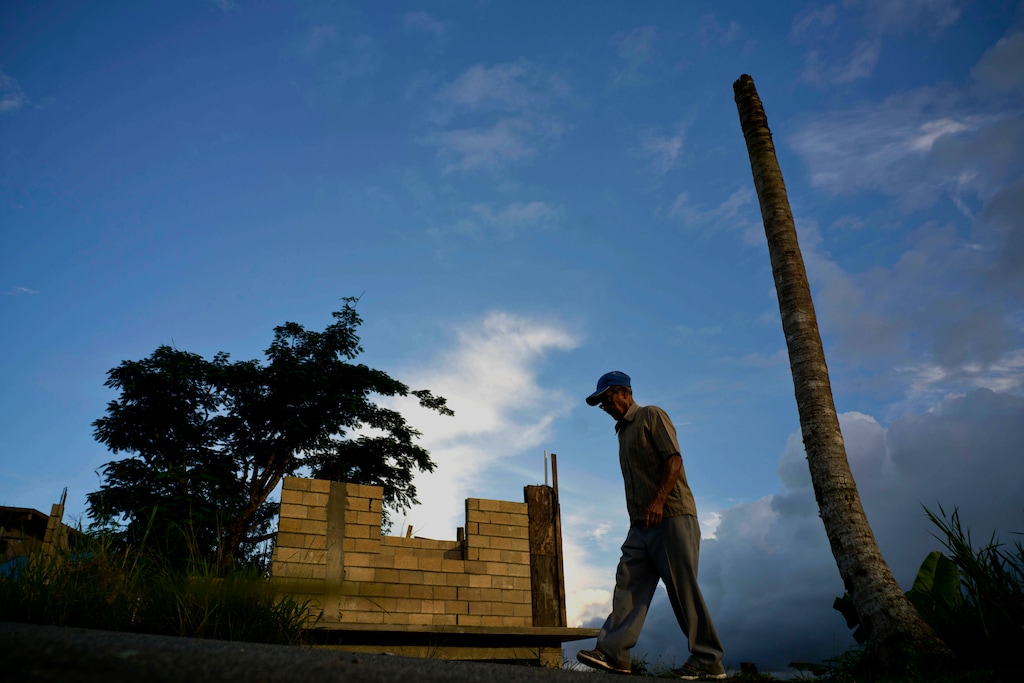 (Ramon Espinosa | AP FILE) In this Sept. 8, 2018, file photo, Ramon Alicea Burgos walks past his palm tree, with its top broken off one year ago by Hurricane Maria one outside his partially rebuilt home in the mountain town of Barranquitas, Puerto Rico. A fight between President Donald Trump and Democrats over hurricane relief for Puerto Rico is imperiling a widely backed disaster aid bill that is a top priority for some of Trump’s southern GOP allies.