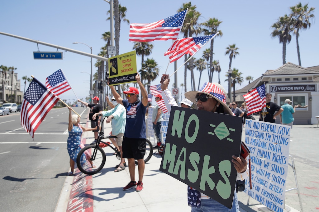 (Marcio Jose Sanchez | AP file photo)  Demonstrators hold signs and U.S. flags as they protest the lockdown and wearing masks Saturday, June 27, 2020, in Huntington Beach, Calif.