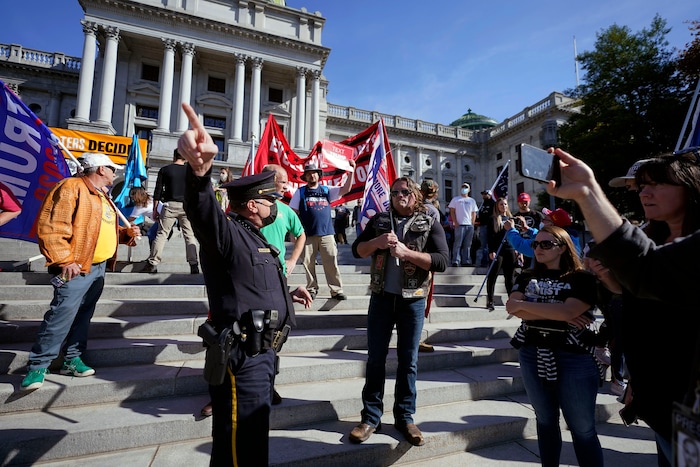 A police officer directs supporters of President Donald Trump away from the Pennsylvania State Capitol Plaza where they did not have a permit to demonstrate, Saturday, Nov. 7, 2020, in Harrisburg, Pa. A permit had been granted to an opposing group. (AP Photo/Julio Cortez)