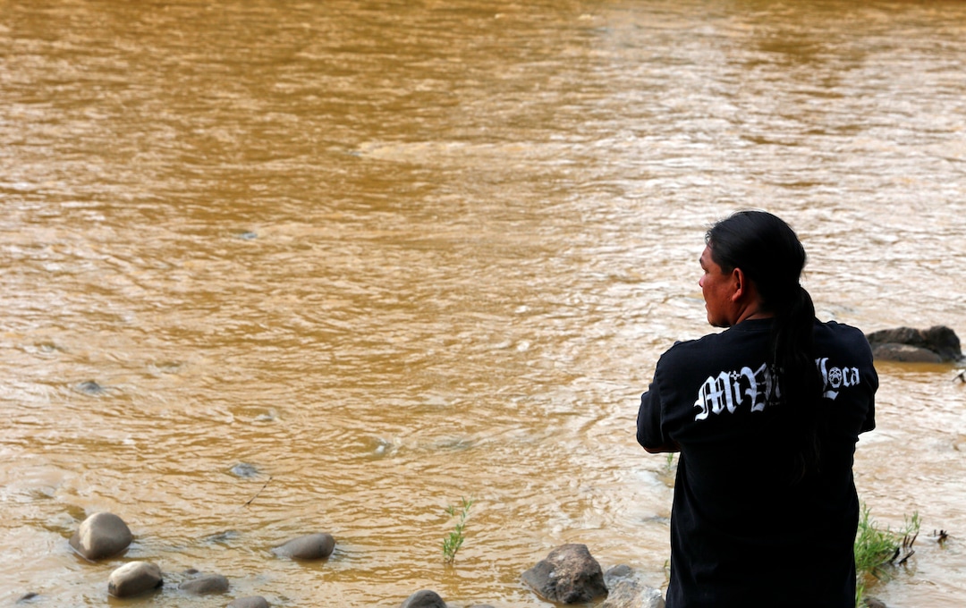 Travis Sells, of Farmington, N.M., looks at the orange sludge from a mine spill upstream flowing past Berg Park in Farmington Saturday, Aug. 8, 2015. About 1 million gallons of wastewater from Colorado's Gold King Mine began spilling into the Animas River on Wednesday when a cleanup crew supervised by the Environmental Protection Agency accidentally breached a debris dam that had formed inside the mine. The mine has been inactive since 1923. (Alexa Rogals/The Daily Times via AP)