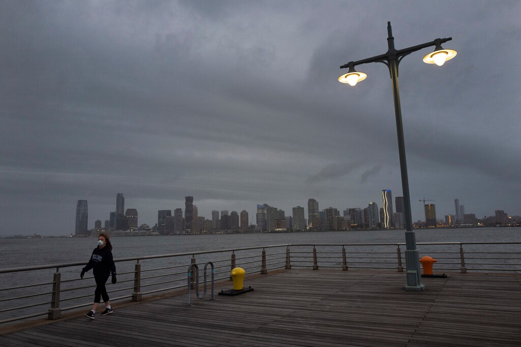 A woman wears a face mask as she walks on Pier 45 in Hudson River Park, Thursday night, April 30, 2020, in New York. As the new coronavirus pandemic upends lives across the United States, it is taking a widespread toll on people's mental health and stress levels. (AP Photo/Mark Lennihan)