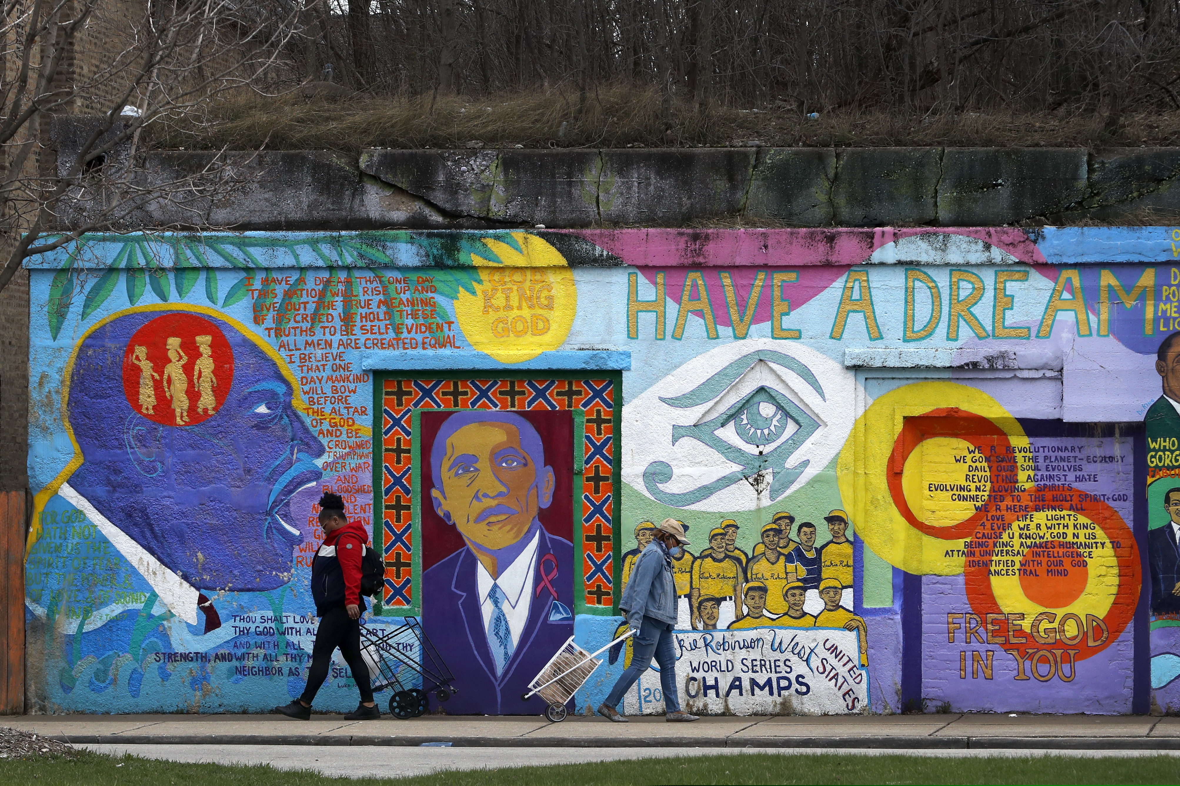 (Charles Rex Arbogast | AP photo) In this April 7 photo, two women pass each other and an African-American mural as they travel to and from a local grocery store on Chicago's Southside. As the coronavirus tightened its grip across the country, it is cutting a particularly devastating swath through an already vulnerable population, black Americans.