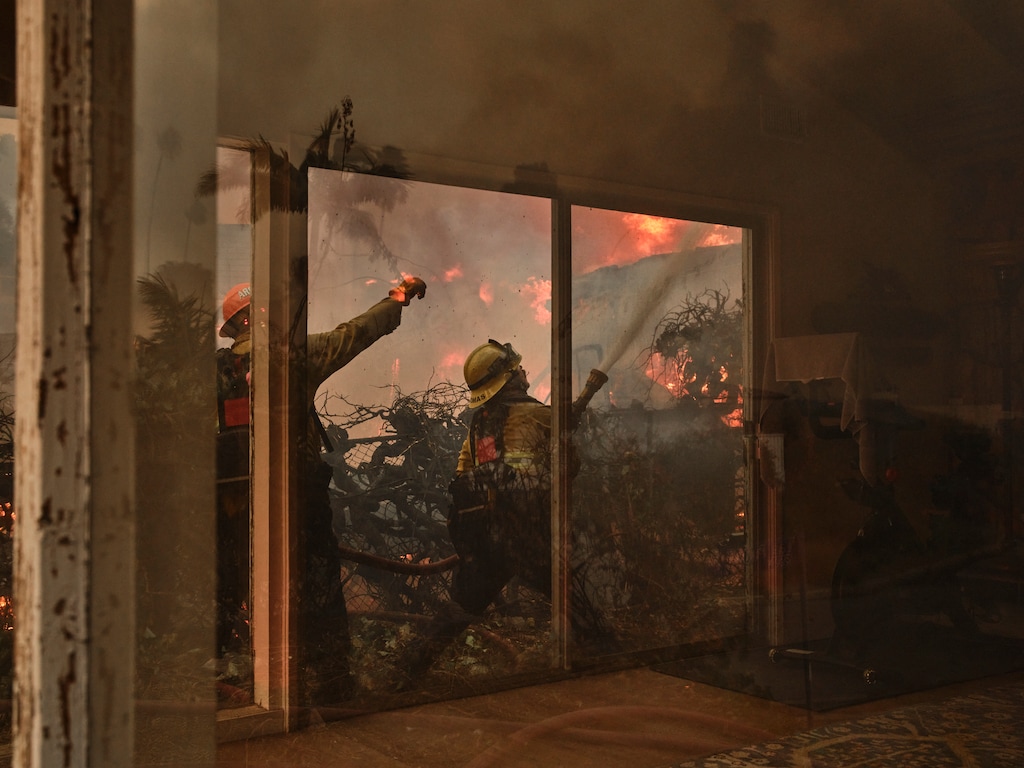 (Philip Cheung | The New York Times) Firefighters work to put out the wildfire in a residential area during the Pacific Palisades fire in Los Angeles, on Tuesday, Jan. 7, 2025. Cars clogged scenic Sunset Boulevard and headed away from the Palisades, a seaside neighborhood on the west side of Los Angeles.