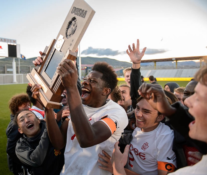 (Trent Nelson | The Salt Lake Tribune)  Judge Memorial players celebrate their win over Morgan High School in the 3A state championship game, Saturday May 12, 2018. Holding the trophy is Ferdinand Bambabate.