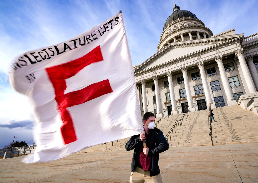(Francisco Kjolseth | The Salt Lake Tribune) Herriman High social studies teacher Michael Stone holds a flag in strong bitter cold winds as educators, parents and other public school advocates rally on the steps of the Utah Capitol on Tuesday, Feb. 22, 2022.