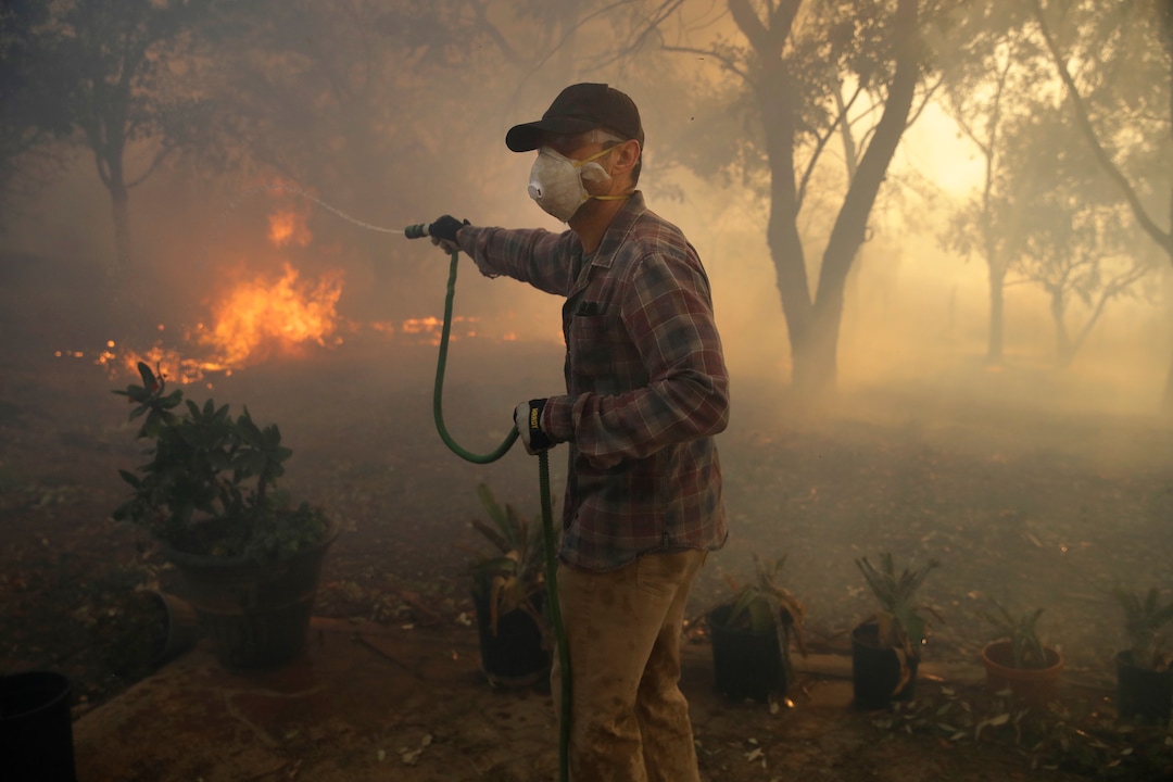 (Marcio Jose Sanchez | AP) Marco Alcaraz uses a garden hose to try to slow down the advance of the Easy fire as it approaches Beth Rivera's property Wednesday, Oct. 30, 2019, in Simi Valley, Calif.  Driven by powerful Santa Ana winds, the brush fire broke out before dawn between the cities of Simi Valley and Moorpark north of Los Angeles and exploded to more than 1,300 acres (526 hectares), threatening 6,500 homes, Ventura County officials said.