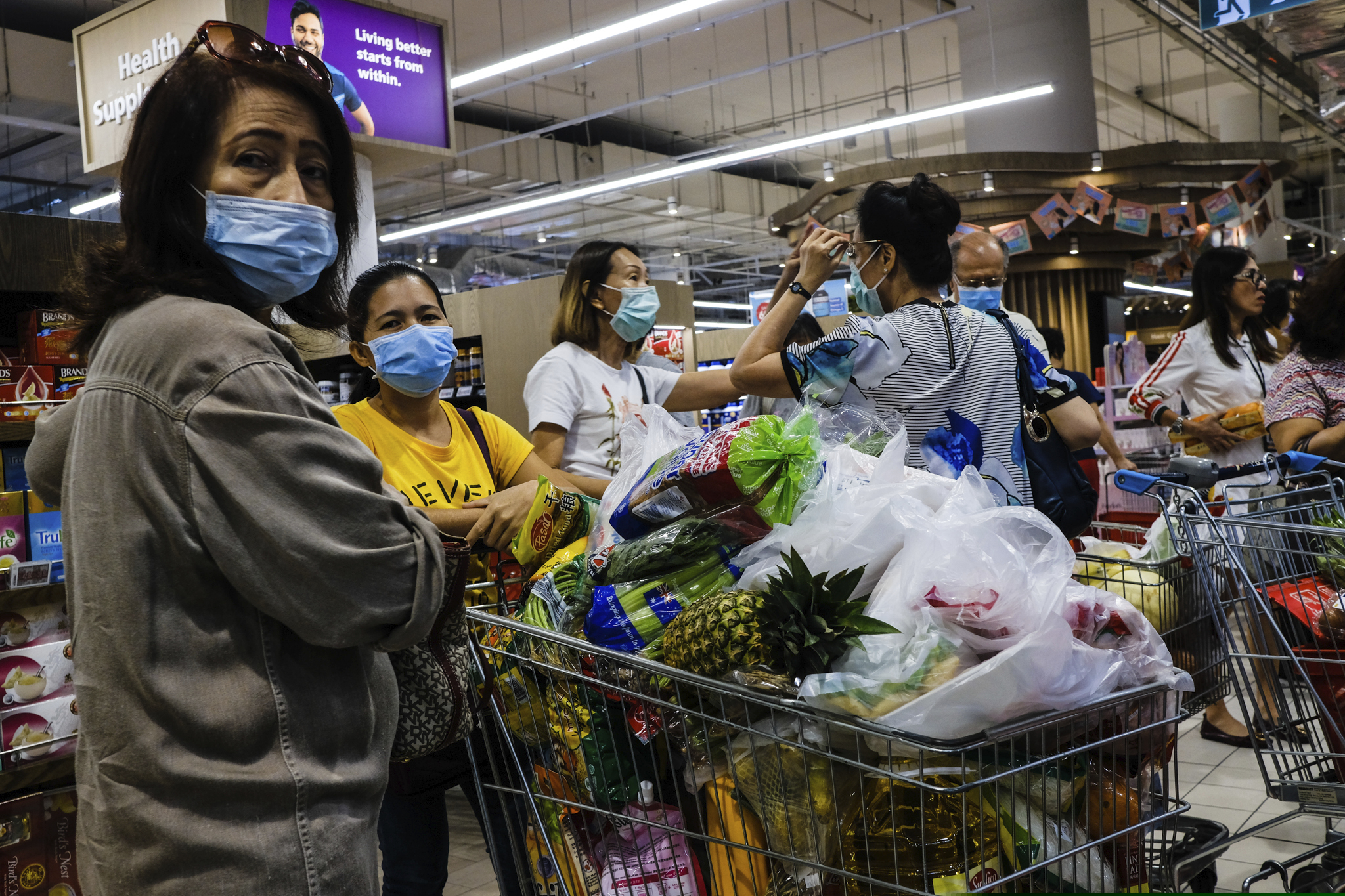 (Ee Ming Toh | The Associated Press) Shoppers wearing face masks with a cart full of food supplies wait in line to pay at a supermarket counter in Singapore, Tuesday, Mar. 17, 2020. Singaporeans were seen buying food supplies in supermarkets following neighboring Malaysia's announcement of a nationwide lockdown from the coronavirus to begin Wednesday which could affect the flow of food supplies to the city state.