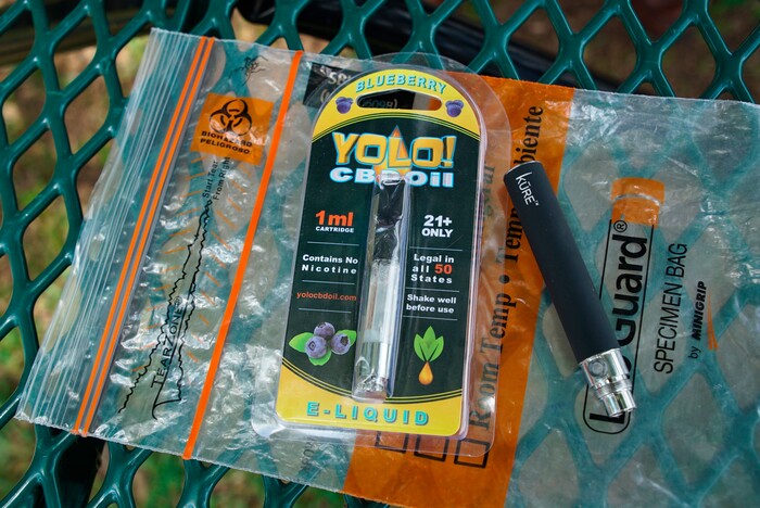 (Allen G. Breed | AP) A Yolo! brand CBD oil vape cartridge sits alongside a vape pen on a biohazard bag on a table at a park in Ninety Six, S.C., on Wednesday, May 8, 2019. Jay Jenkins says two hits from the vape put him in a coma and nearly killed him in 2018. Lab testing commissioned by The Associated Press shows this cartridge and several other vapes marketed as delivering CBD instead contained synthetic marijuana, a street drug commonly known as K2 or spice.