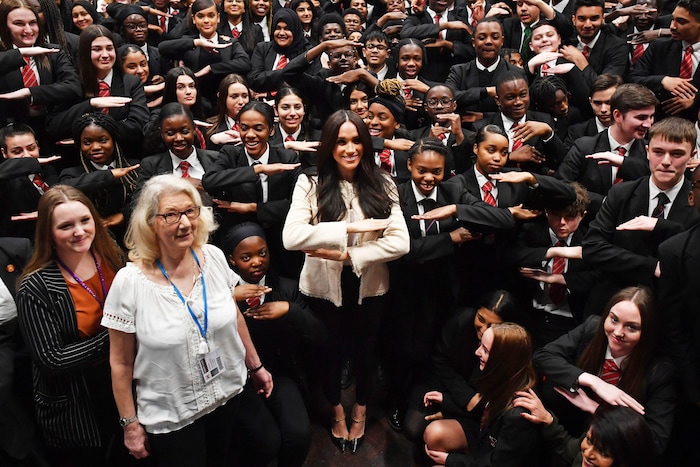 Britain's Meghan, Duchess of Sussex, center, poses with school children making the "equality" sign following a school assembly during a surprise visit to the Robert Clack Upper School in Dagenham, Essex, in eastern London, to celebrate International Women's Day, Friday, March 6, 2020. Meghan visited the school, addressing pupils in an assembly ahead of the worldwide celebration of women's achievements on Sunday. (Ben Stansall/Pool via AP)