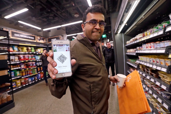 Amazon employee Krishna Iyer shows off an Amazon Go app as he shops in the store, Monday, Jan. 22, 2018, in Seattle. The store allows shoppers to scan their smartphone with the Amazon Go app at a turnstile, pick out the items they want and leave. The online retail giant can tell what people have purchased and automatically charges their Amazon account. (AP Photo/Elaine Thompson)