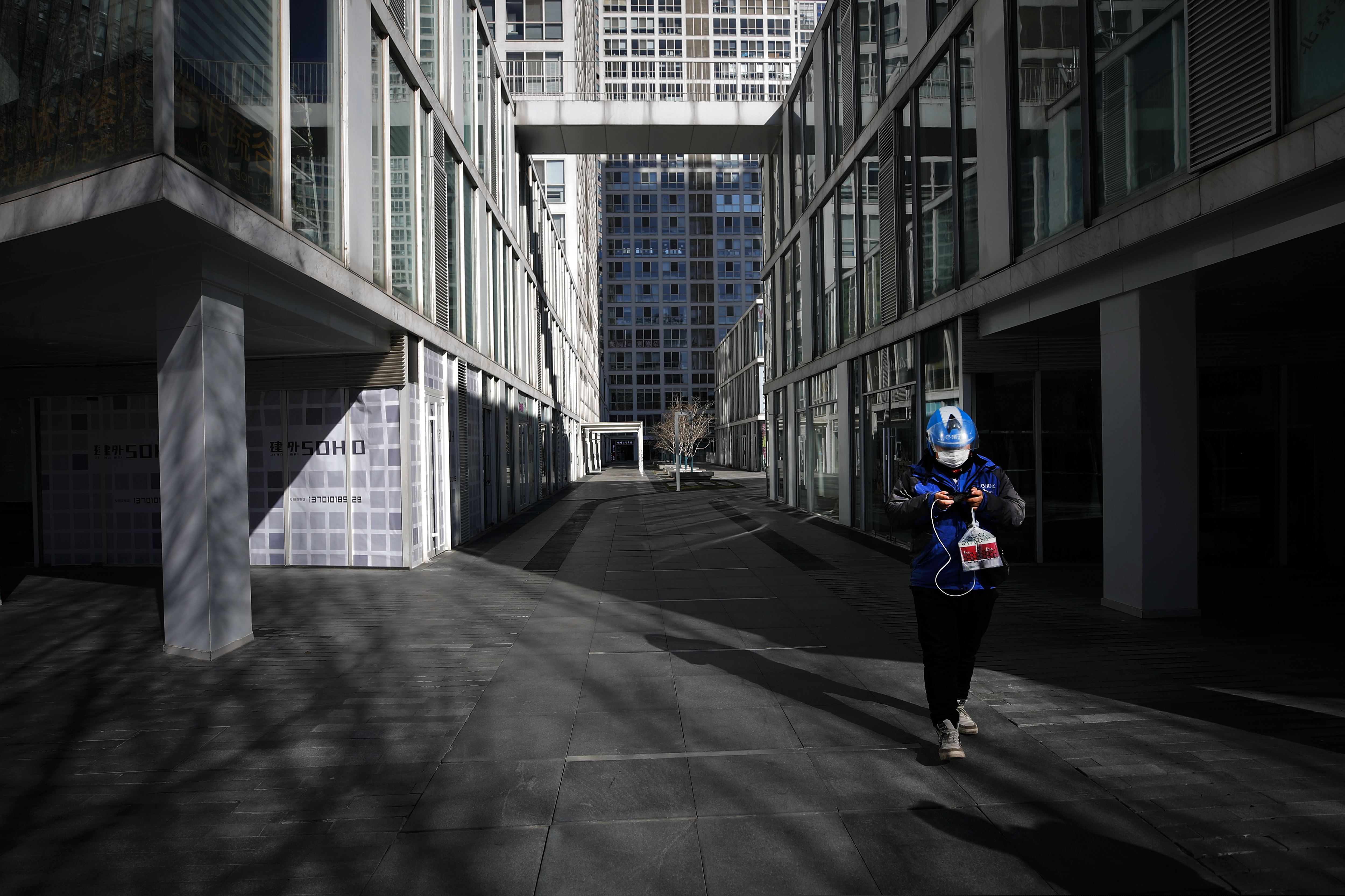 (Andy Wong | AP)  A food delivery worker passes a deserted compound of a commercial office building during the lunch break in Beijing, Monday, Feb. 17, 2020. Chinese authorities on Monday reported a slight upturn in new virus cases and hundred more deaths, as the military dispatched hundreds more medical workers and extra supplies to the city hit hardest by the 2-month-old outbreak.