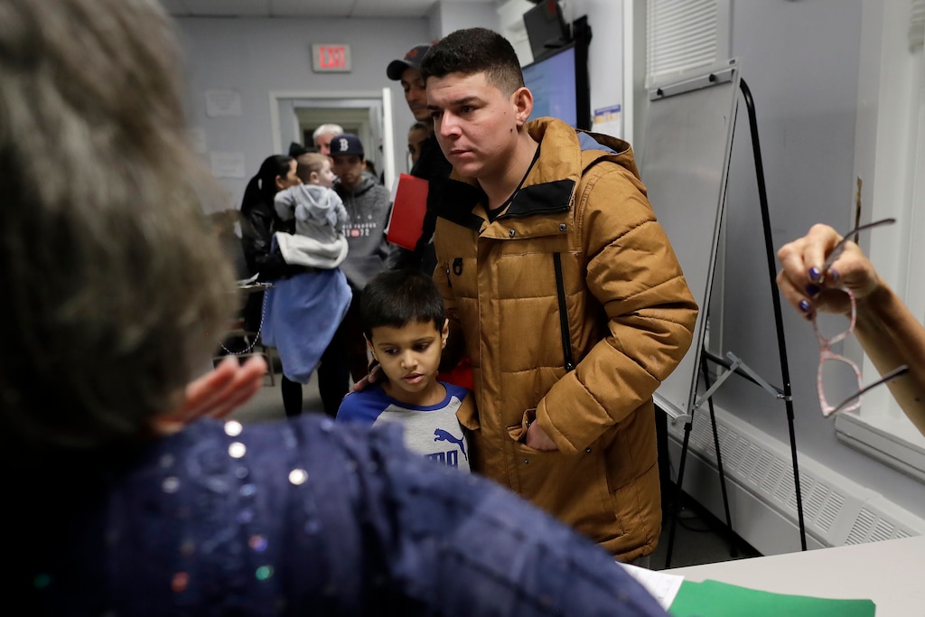 (Steven Senne | AP) In this Wednesday, Dec. 4, 2019 photo, Helison Alvarenga, of Brazil, center right, and his 6-year-old son, David, center left, move away from a reception table after speaking with volunteers at the New England Community Center, in Stoughton, Mass. Alvarenga, a 26-year-old from the Brazilian state of Minas Gerais, arrived in Massachusetts about four months ago after crossing the Mexican border at Juarez with his 24-year-old wife, Amanda, and his son David. The family was at the community center Dec. 4 to apply for new Brazilian passports, which Alvarenga says were seized by border officials.