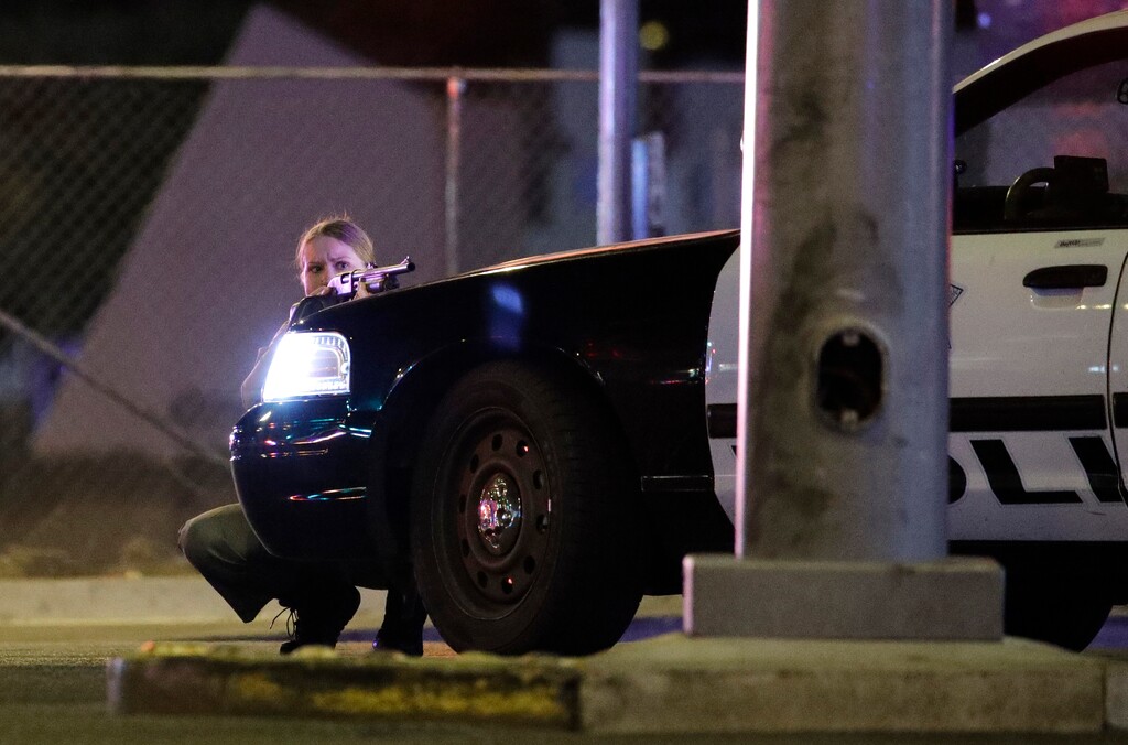 A police officer takes cover behind a police vehicle during a shooting near the Mandalay Bay resort and casino on the Las Vegas Strip, Sunday, Oct. 1, 2017, in Las Vegas. (AP Photo/John Locher)