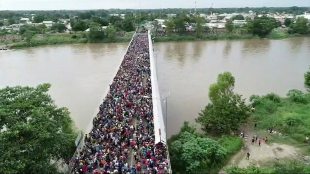 This Oct. 19, 2018 frame grab from video provided by Televisa, shows migrants bound for the U.S.-Mexico border waiting on a bridge that stretches over the Suchiate River, connecting Guatemala and Mexico, in Tecun Uman, Guatemala. The gated entry into Mexico via the bridge has been closed. The U.S. president has made it clear to Mexico that he is monitoring its response. On Thursday he threatened to close the U.S. border if Mexico didn't stop the caravan. (Televisa via AP)