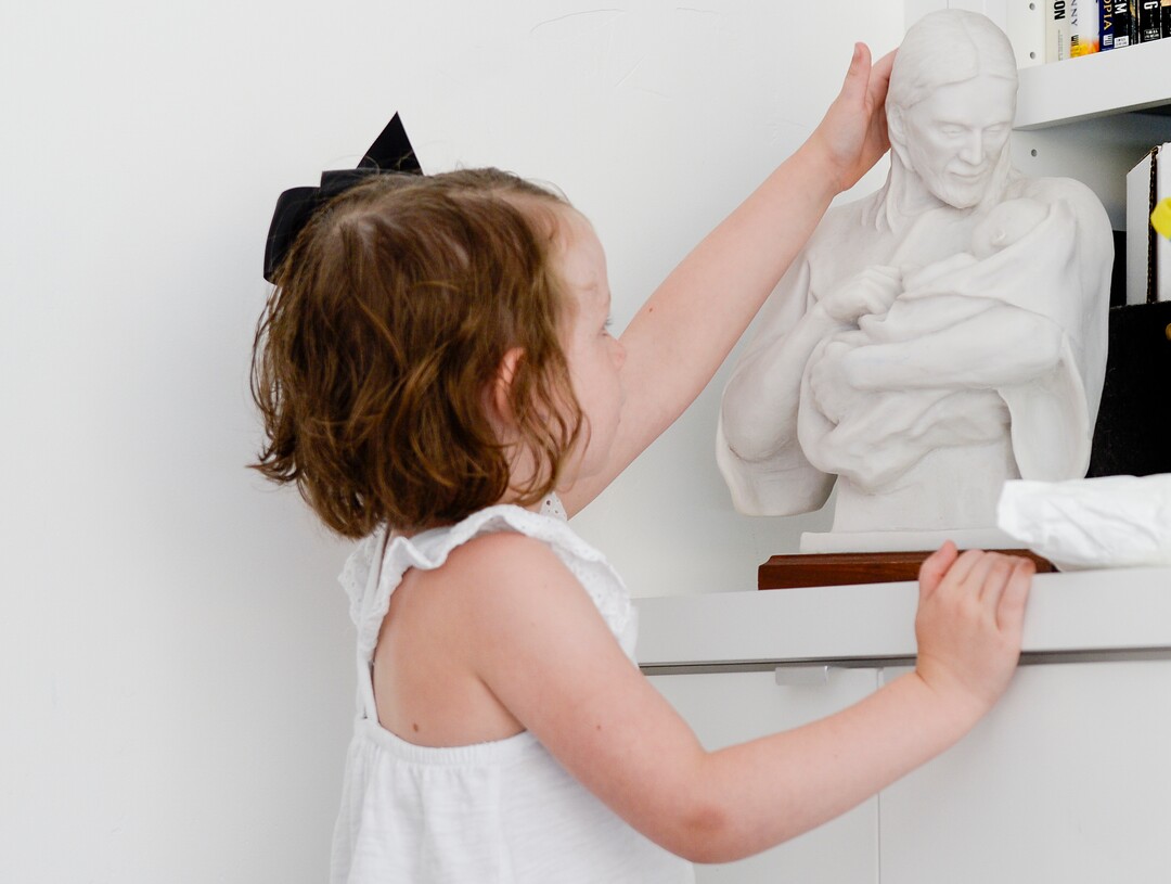 (Leah Hogsten  |  The Salt Lake Tribune) Ramsi Stoker's daughter Revali Stoker, 4, caresses a statue of Jesus holding a baby in the living room of their home on Friday, Aug. 2, 2019. Ramsi Stoker, 39, and her husband, Brian, not pictured, struggled with unexplained infertility until seeking help from the Utah Fertility Center and the Footsteps to Fertility program in 2012.