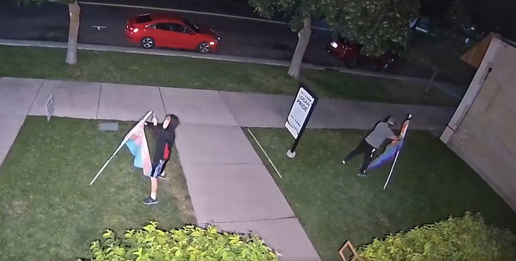 Two masked individuals vandalizing and stealing pride flags outside Logan Pride House at night.