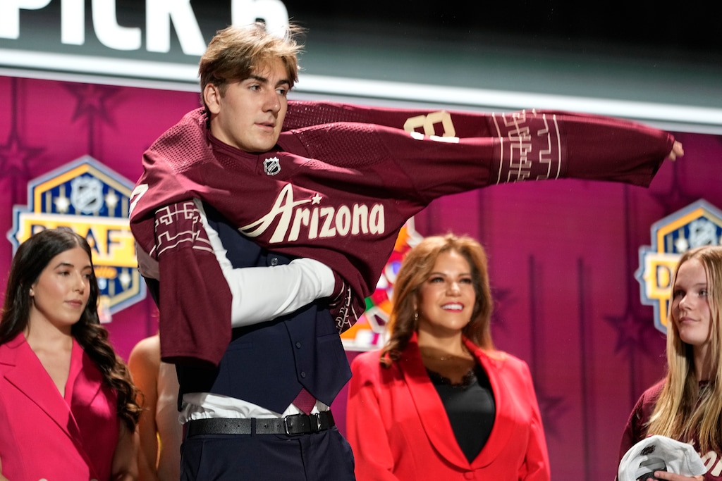 Dmitriy Simashev puts on a Arizona Coyotes jersey after being picked by the team during the first round of the NHL hockey draft Wednesday, June 28, 2023, in Nashville, Tenn. (AP Photo/George Walker IV)